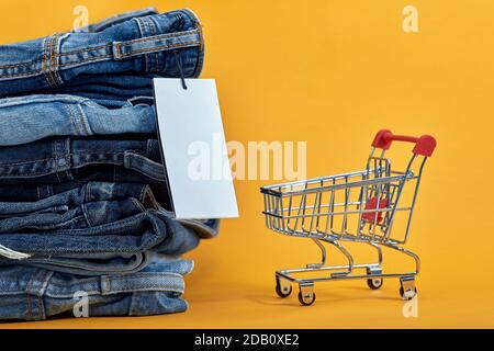 Une pile de jeans bleus avec une étiquette blanche sur fond jaune. Chariot avec cubes multicolores. Ventes consép Banque D'Images