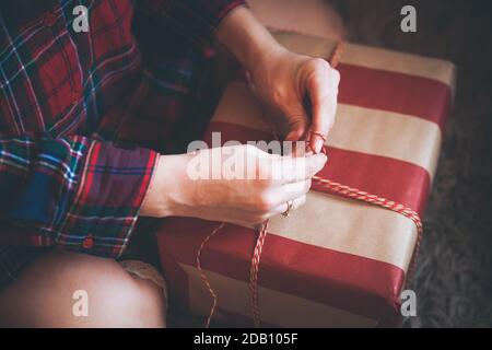 Femme emballant des cadeaux de Noël assis sur le sol dans une chemise à carreaux rouges. Ambiance de Noël rustique. Banque D'Images