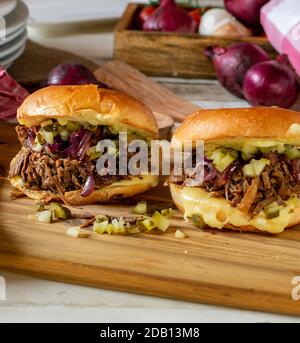 hamburger de bœuf tiré maison avec oignons rouges caramélisés, cornichons et fromage sur une planche de bois Banque D'Images