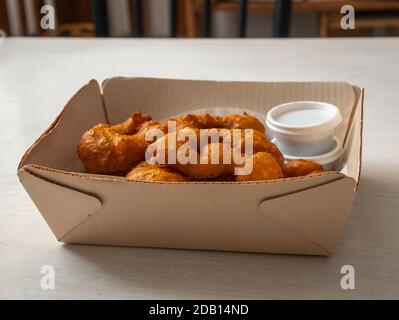 Picarones, desserts péruviens à base de squash et de patate douce, servis sous forme de Donut avec sirop à base de Panela dans une boîte en carton sur table blanche Banque D'Images