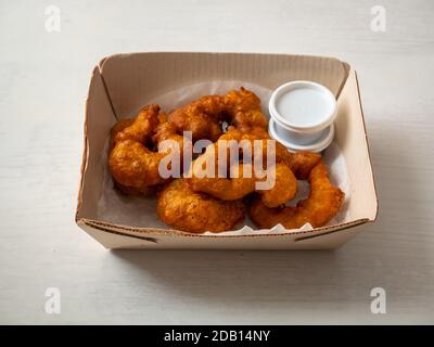 Picarones, desserts péruviens à base de squash et de patate douce, servis sous forme de Donut avec sirop à base de Panela dans une boîte en carton sur table blanche Banque D'Images