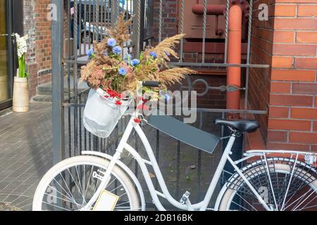 Vélo blanc avec un panier de fleurs sauvages dans une rue de la ville. Espace de copie, mise au point sélective. Banque D'Images