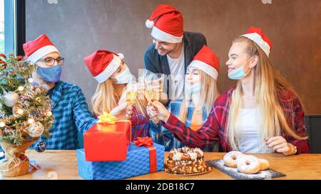 Un groupe de jeunes amis heureux avec des masques pour le visage fêtent Noël ensemble, boire du champagne à l'isolement à la maison Banque D'Images