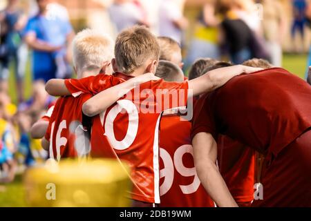 Enfants en équipe sportive. Enfants avec un entraîneur de football junior qui se mêlent en cercle. Les garçons font équipe avec des chemises rouges qui se réunissent pour élaborer des stratégies, motiver ou caser Banque D'Images