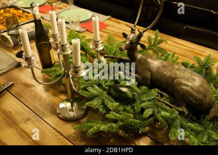 Dîner de Noël sur une table en bois avec des branches de pin, un lustre et une bouteille de vin rouge Banque D'Images