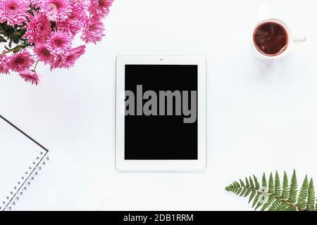 Tablette, ordinateur portable, tasse de café, bouquet de chrysanthèmes roses et feuilles de fougères sur fond blanc. Espace de travail confortable, vue sur le dessus, espace de copie. Banque D'Images