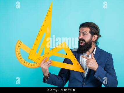 mesure et taille. bon enseignant mature tenant un triangle et un outil de rapporteur. homme barbu ingénieur travaille avec la règle. préparez-vous pour l'examen de géométrie. architecte ou professeur de mathématiques. retour à l'école. Banque D'Images