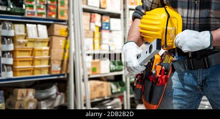 L'électricien du magasin de pièces électriques maintient le niveau à la main, casque avec lunettes de protection. Industrie de la construction, système électrique. Banque D'Images