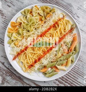 Différents types de pâtes dans une assiette blanche sur fond gris en bois. Décoré de poivron rouge, de fromage et d'un morceau de menthe. Vue de dessus Banque D'Images