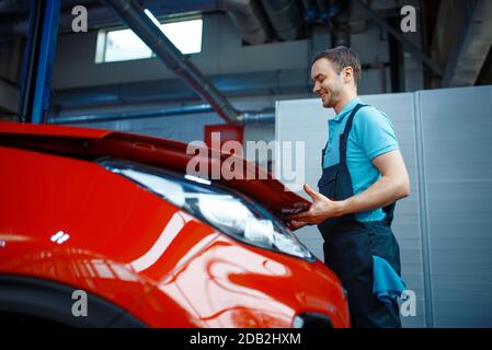 L'employé en uniforme ouvre le capot du véhicule, la station-service. Contrôle et inspection automobiles, diagnostic et réparation professionnels Banque D'Images