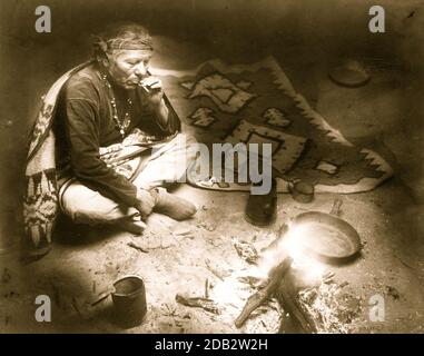 Navajo Indien, assis près d'un feu de camp, fumer la cigarette. Banque D'Images