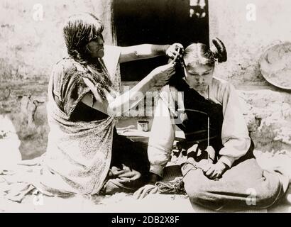 Agenouiller la femme Hopi peignant et arranger les cheveux de la jeune fille. Banque D'Images