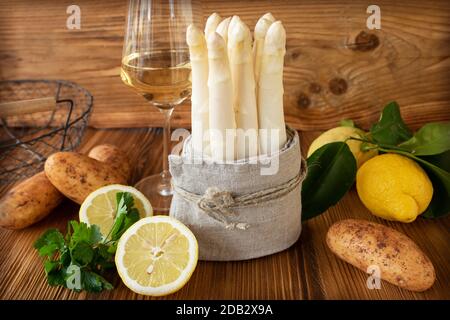 Ensemble d'asperges blanches dans un linge de maison avec des potatos frais et du citron sur une table rustique en bois. Encore plus de vie avec du vin blanc et une courte profondeur de mise au point. Co Banque D'Images