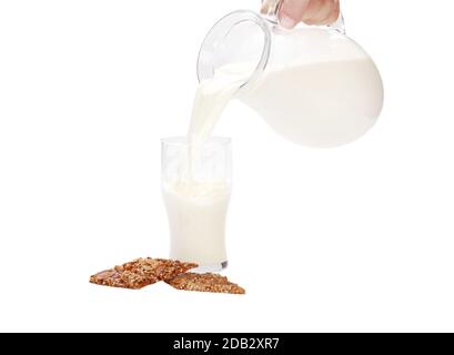 Une personne qui verse du lait dans une tasse de verre avec des biscuits isolé sur un fond blanc Banque D'Images