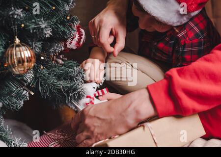 Gros plan des mains des enfants et des pères accrochant un jouet décoratif sur la branche de l'arbre de Noël. Banque D'Images