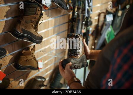 Homme choisissant des bottes pour les chasseurs à la vitrine dans la boutique d'armes à feu. Euqipment et fusils sur le stand dans le magasin d'armes, la chasse et le sport de tir hobby Banque D'Images