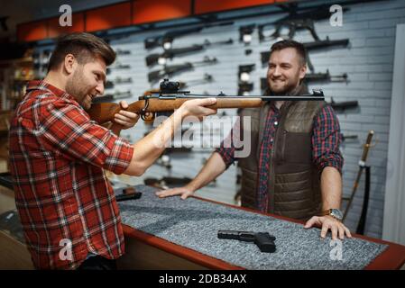 Man vise avec un nouveau fusil, vendeur au comptoir dans la boutique d'armes à feu. Homme personne achetant une arme en magasin, chasse et sport de tir hobby Banque D'Images