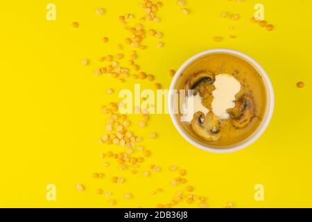 La soupe de pois aux champignons dans une assiette rose est sur fond jaune, autour de la dispersion des graines de lentilles. Banque D'Images