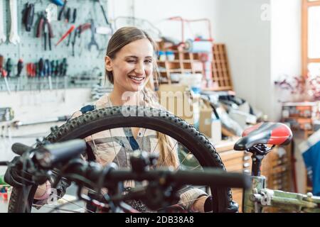 Très heureux mécanicien vélo femme regardant à travers la roue de bicyclette Banque D'Images