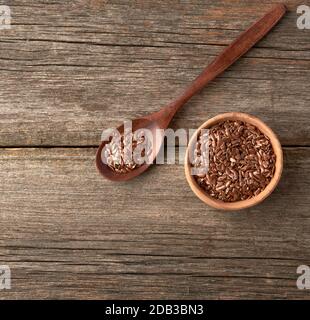 graines de lin brun sec dans une cuillère en bois brun sur une table en bois gris à partir de vieux planches, vue de dessus Banque D'Images