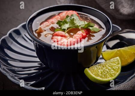 Délicieuse soupe de poisson aux crevettes dans un bol bleu foncé servi avec du persil et du citron vert sur fond gris foncé. Une alimentation saine. Menu de fruits de mer Banque D'Images