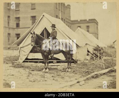 Le major-général Joseph Hooker, portrait en longueur, assis sur un cheval, face à la gauche, portant un uniforme militaire, deux tentes et un grand bâtiment en arrière-plan. Banque D'Images