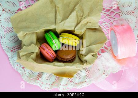 Macarons jaune, rose, vert et marron dans le pack artisanal sur fond pinc. Vues de dessus Banque D'Images