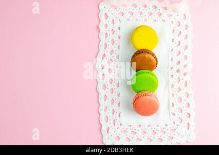 Plusieurs macarons multicolores aux couleurs pastel sur une serviette blanche sur fond rose. Banque D'Images