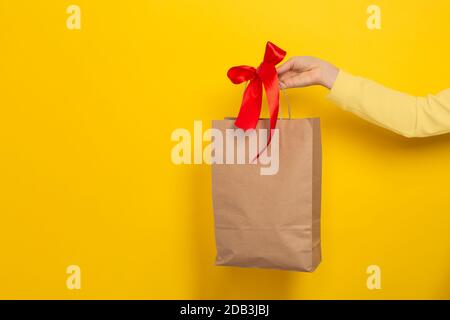 Grande poche cadeau pour femme en papier brun artisanal avec noeud rouge sur fond jaune. Concept cadeau, cadeau ou e-shopping. Bannière avec copie s Banque D'Images