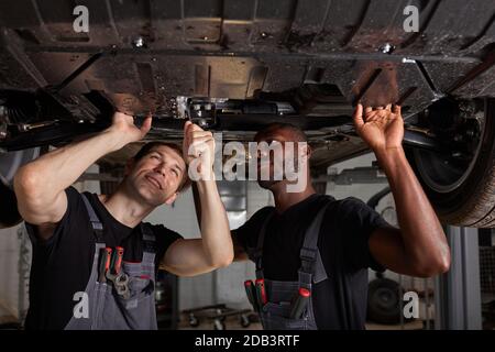 deux mécaniciens interraciaux divers vérifiant le fond de la voiture en service auto, coopérer, travailler ensemble Banque D'Images