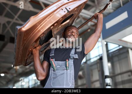 afro american auto mécanicien va changer partie séparée de l'automobile. tenir le métal lourd dans la main Banque D'Images