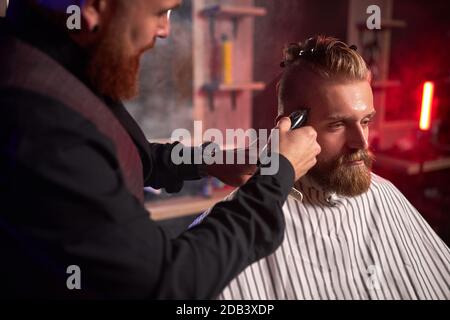 coiffeur homme confiant coupe les cheveux à l'homme élégant et élégant assis dans le salon, les jeunes hommes apprécient le processus de coupe Banque D'Images