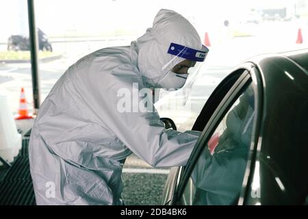 Travailleur médical dans l'EPI exécutant un écouvillon nasal et de gorge sur une personne dans le véhicule à travers la fenêtre de voiture, centre de test mobile COVID-19. Turin, Italie - 2 novembre Banque D'Images