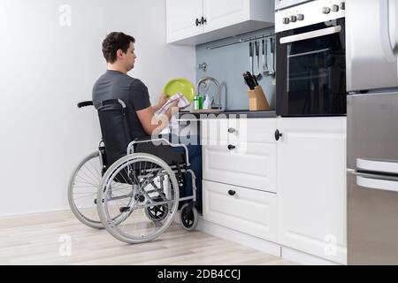 Homme handicapé assis sur fauteuil roulant et laver la vaisselle dans la cuisine Banque D'Images