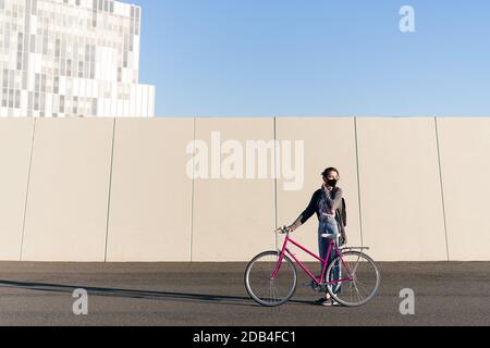 jeune fille avec un vélo rétro rose à la ville en ajustant son masque protecteur, concept de vie active, protection contre le covid et durable urbain m. Banque D'Images