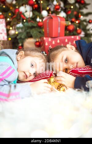 Une petite fille dans les vêtements de la maison est couché sous l'arbre de Noël près des boîtes avec des cadeaux sur l'oreiller et des rêves. Lumières des guirlandes, le befo de nuit Banque D'Images