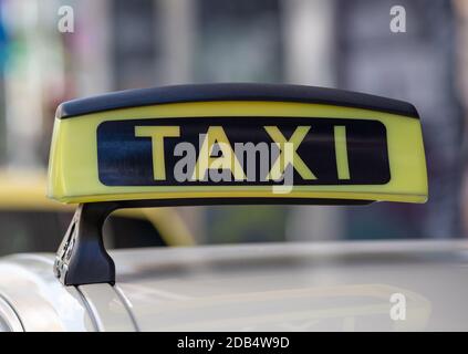 Panneau de taxi sur un toit de voiture, texte jaune et noir, vue rapprochée, taxi sur la rue de la ville à l'heure de la journée attendant le passager, flou paysage urbain arrière Banque D'Images