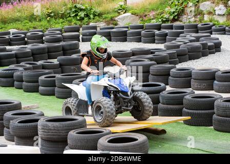 Jeune fille à vélo quad autour d'une piste entre pneus empilés pour le montage de sécurité d'une petite rampe comme elle conduit dans un concept de sport récréatif Banque D'Images