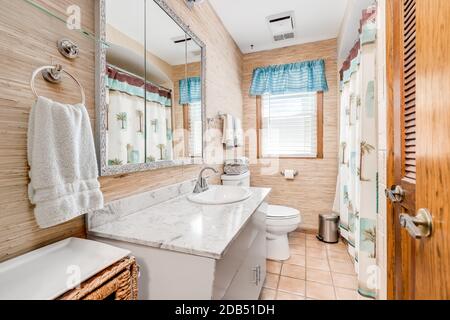 Ancienne salle de bains avec papier peint en bois, comptoir blanc et rideau de douche à motifs. Banque D'Images