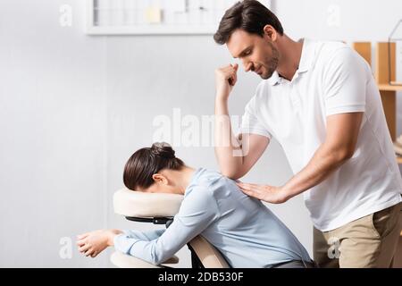 Masseuse souriante massante femme d'affaires dos avec coude dans le bureau arrière-plan flou Banque D'Images