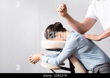 Vue latérale de la femme massante dos avec coude, assise sur une chaise de massage sur fond blanc Banque D'Images