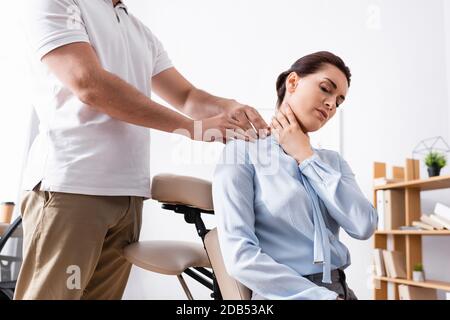 Massothérapeute massant l'épaule douloureuse de femme d'affaires assis sur le massage chaise au bureau sur fond flou Banque D'Images