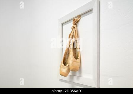 de vieilles chaussures de ballerine accrochées dans un cadre sur un mur blanc, comme un souvenir de la carrière d'une ballerine. Banque D'Images