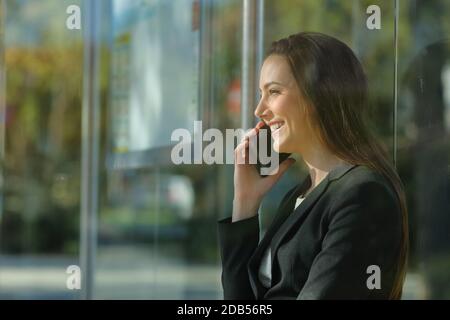 Profle d'une heureuse femme de direction parlant sur smartphone en attendant un arrêt de bus Banque D'Images