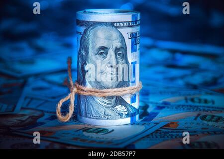 Un rouleau de dollars sur l'arrière-plan de la dispersion hundred dollar bills in blue light Banque D'Images