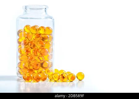 Les capsules jaunes dispersés à partir d'un bocal en verre sur un fond blanc Banque D'Images