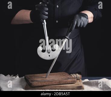 la cuisson masculine en gants en latex noir uniforme et noir contient un grand couteau vintage pour la viande et les légumes et un aiguiseur en métal pour les couteaux, le ba noir Banque D'Images