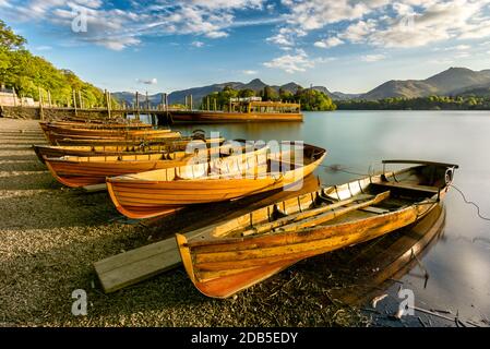 Bateaux d'aviron en bois alignés sur le rivage étant illuminés avec la lumière dorée du soleil couchant. Derwentwater, Lake District, Royaume-Uni. Banque D'Images