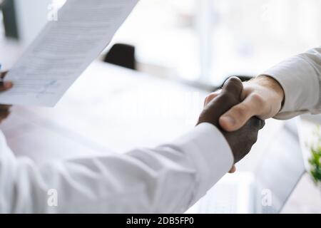 Vue de dessus de la poignée de main de l'homme d'affaires africain et de l'homme d'affaires caucasien sur le lieu de travail, gros plan. Banque D'Images