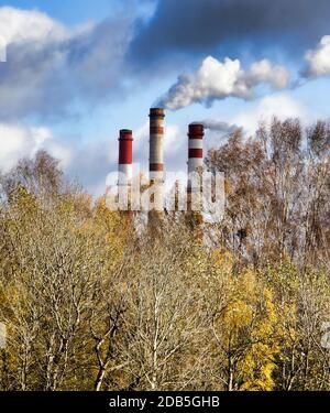 Usine industrielle avec tuyaux et fumée à l'arrière différents types d'arbres à feuilles caduques avec feuillage de couleur changeée en automne, temps ensoleillé en automne Banque D'Images